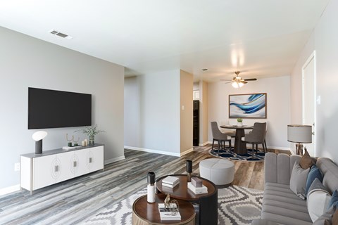 A modern living room with a grey sofa, a wooden coffee table, and a television on a white cabinet.